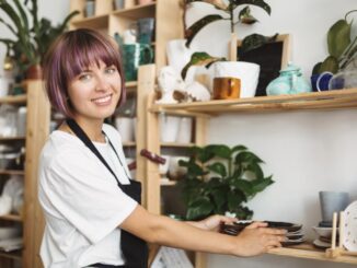 Woman organizing pottery on wooden shelves.