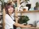 Woman organizing pottery on wooden shelves.