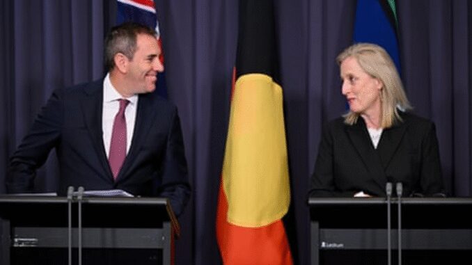 Two people speaking at podiums, flags behind.