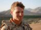 Soldier smiling with mountainous landscape background.