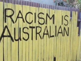 Yellow fence with "Racism is Australian" graffiti.