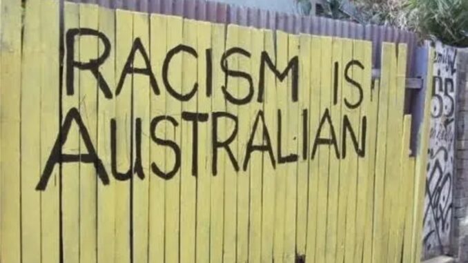 Yellow fence with "Racism is Australian" graffiti.