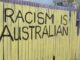 Yellow fence with "Racism is Australian" graffiti.