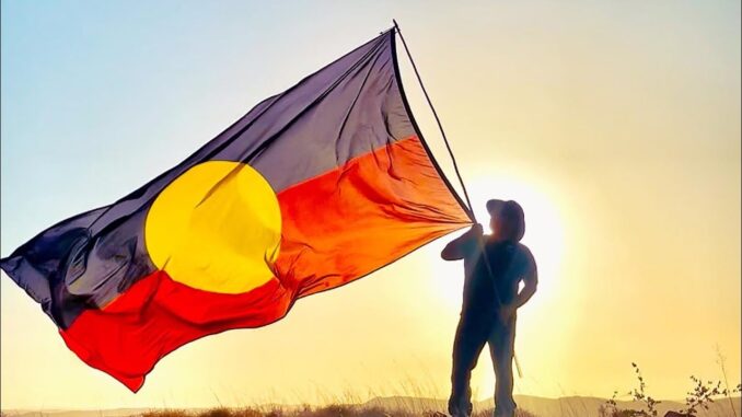Person holding Aboriginal flag against sunrise.