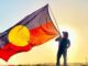 Person holding Aboriginal flag against sunrise.