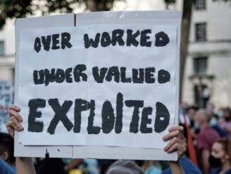 Protest sign: "Overworked, Undervalued, Exploited.