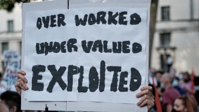 Protest sign: "Overworked, Undervalued, Exploited.
