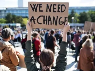 Person holding "We Need A Change" sign.