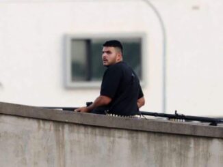 Man standing on rooftop with a rifle.