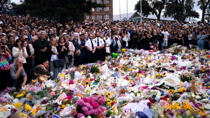 Crowd gathers around memorial with flowers.