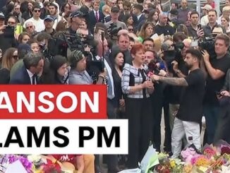 Crowd gathered with media, floral tributes visible.