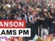Crowd gathered with media, floral tributes visible.