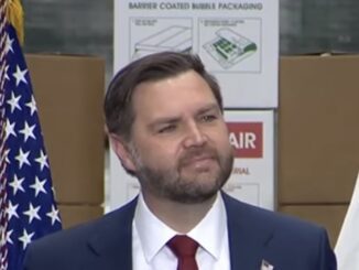 Man speaking at an event with flags.