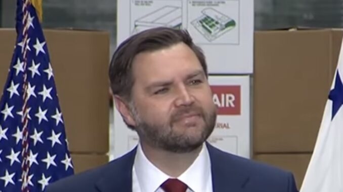 Man speaking at an event with flags.