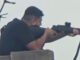 Person aiming rifle from a rooftop.
