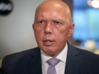 Man in suit speaking, blurred background.