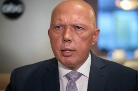 Man in suit speaking, blurred background.
