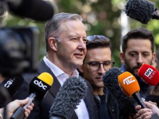 Man speaking to reporters with microphones outside.