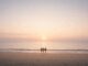 Sunset beach scene with four people standing.