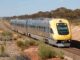 Yellow train traveling through rural landscape.