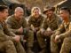 Soldiers sitting outdoors, smiling, holding mugs.