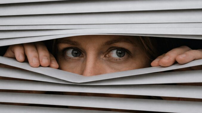 Person peering through partially opened blinds. Person peering through partially opened blinds.