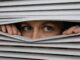 Person peering through partially opened blinds.