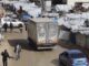 Street with vehicles and tents, crowded scene.