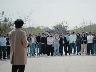 Person speaking to a large outdoor crowd.