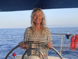 Smiling woman steering sailboat on ocean.