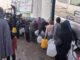 People collecting water from large containers.