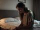 Woman sitting on bed, looking pensive.