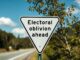 Sign reading "Electoral oblivion ahead" on roadside.