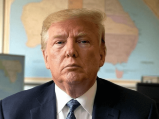 Older man wearing suit seated before world map