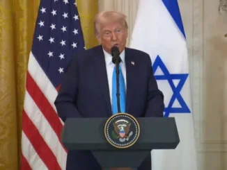 Man speaking at podium with two flags.
