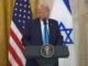 Man speaking at podium with two flags.
