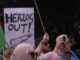 Protesters holding signs and phones at rally.
