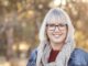 Smiling woman outdoors with glasses and scarf.