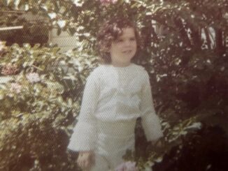 Child standing in garden with flowers.