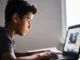 Boy using laptop by a window.