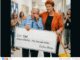 Man receives large check, surrounded by people.