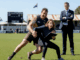 Rugby player and woman on field, clipboard.