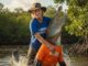 Person wrestling alligator in swampy water.