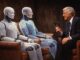 Man interviewing two humanoid robots on stage.