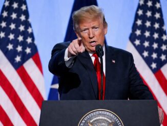 Speaker pointing with American flags behind podium.
