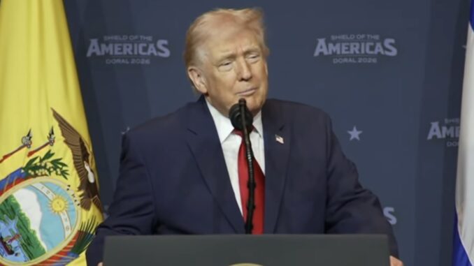 Older man at podium with yellow flag backdrop