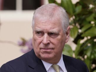 Man in suit standing outdoors, looking sideways.