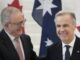 Two men in suits smiling beside national flags