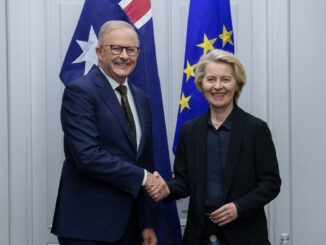 Two people shaking hands, flags behind them.