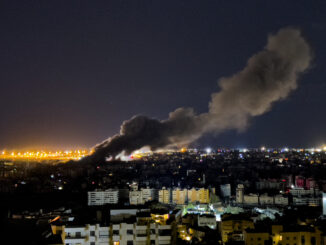 Cityscape at night with rising smoke plume.